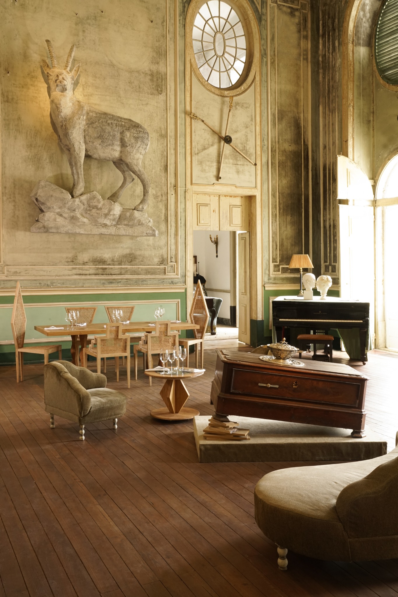 Sunlit interior of Palácio do Grilo, with a horned animal sculpture, circular window, piano and antique furniture